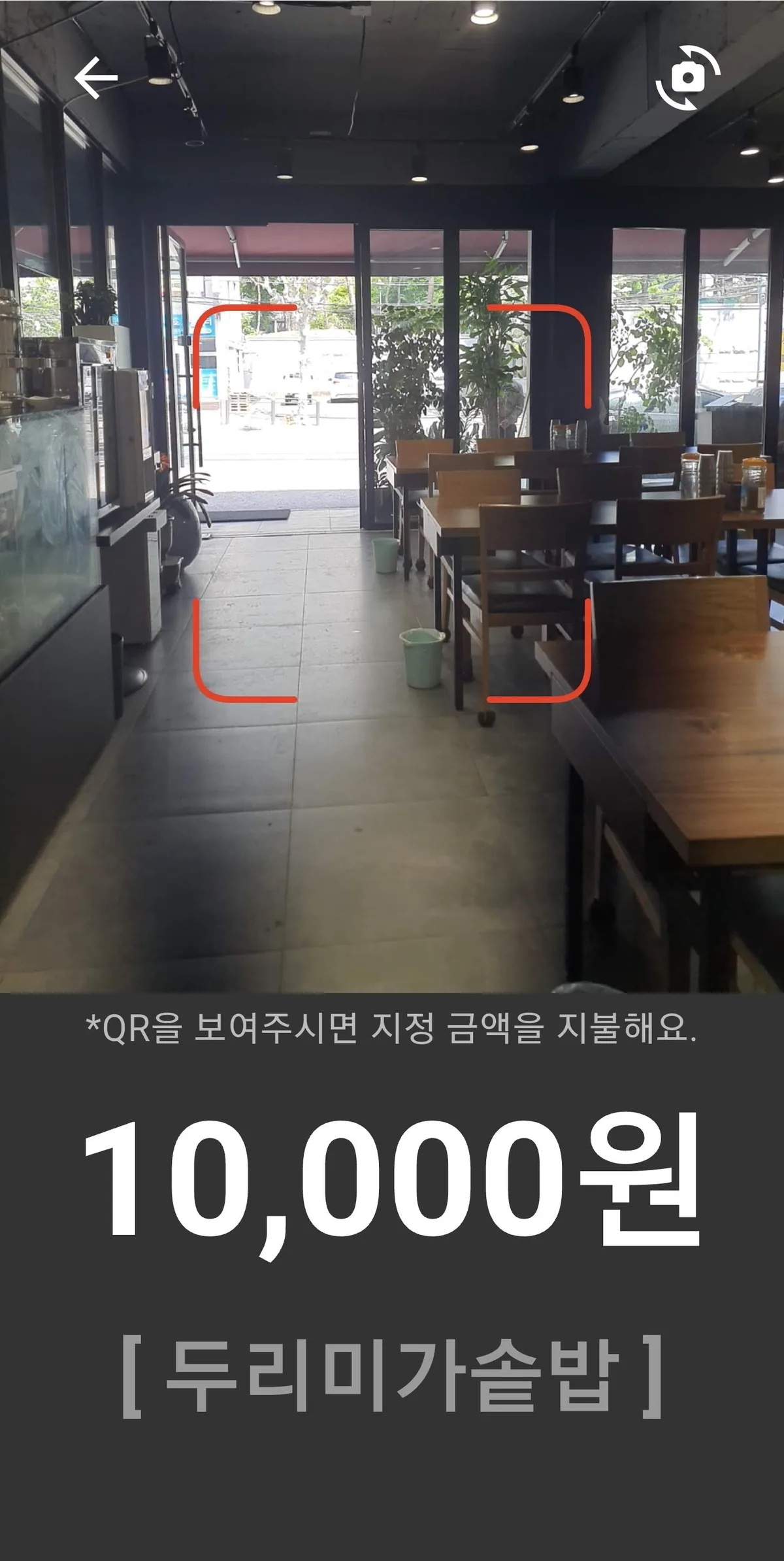 인포 데스크 거치대에 물려 있는 스마트폰 스캐너 화면 — QR을 보여주시면 지정 금액을 지불해요, 10,000원, 두리미가솥밥
